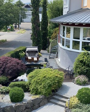 A residential property with a curved house, a small pond, and a garden with various shrubs and a bench. - Cozy vacation apartment on the outskirts of the village (Rüdesheim am Rhein)