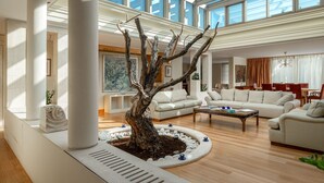 Amplio salón con una gran escultura de árbol, sofás blancos y un techo alto con tragaluces.