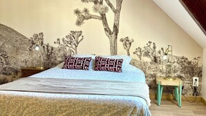 Ein Schlafzimmer mit Bett, Nachttisch, Lampe und Wandgemälde.