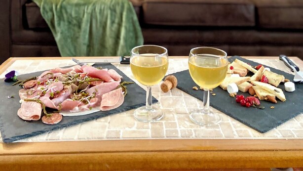 Ein Esstisch mit einer Wurstplatte, zwei Gläsern Weißwein und einer braunen Ledercouch im Hintergrund.
