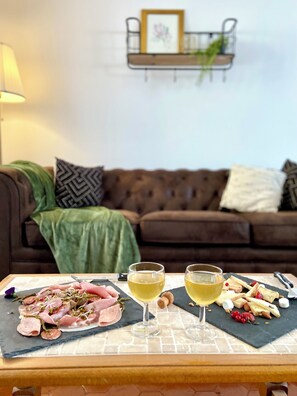 A dining table with a charcuterie board, two glasses of white wine, and a brown leather couch in the background. - La maison des Hortillonnages, countryside in the heart of the city (Amiens)