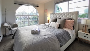 Een slaapkamer met een groot bed, een plafondventilator, een raam met uitzicht en een nachtkastje met een lamp.