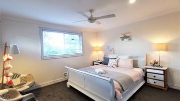 A bedroom with a bed, bedside tables, a ceiling fan, a window, and a chair.