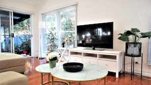 Een moderne woonkamer met een flatscreen televisie, een salontafel, een bank en een potplant.