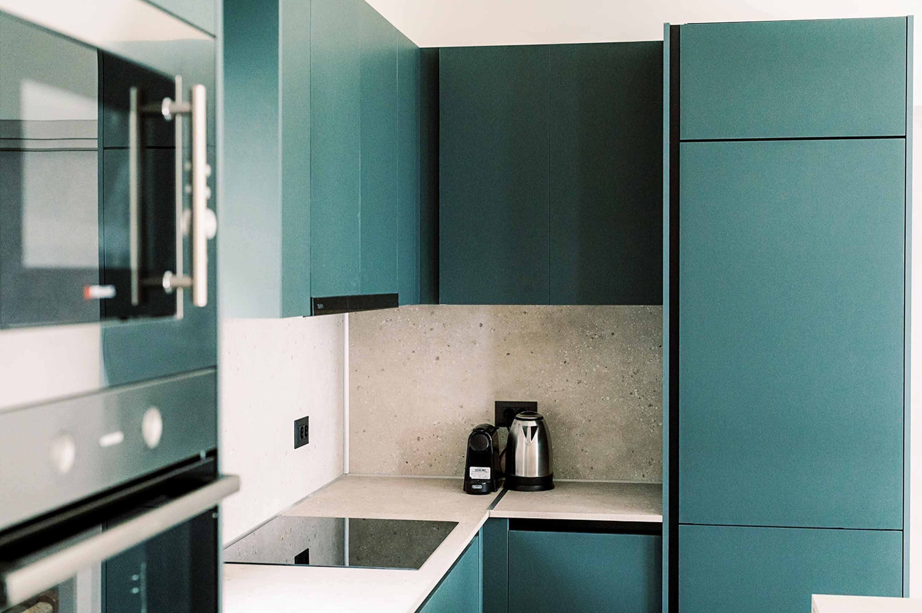 A modern kitchen with teal cabinetry, a built-in oven, and a coffee maker on the countertop.