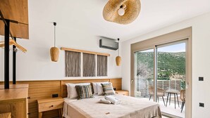 A bedroom with a large bed, wooden headboard, bedside tables, a wardrobe, and a balcony with chairs. - Villa Ieros - Three Bedroom Villa, Sleeps 6 (Ionian Islands)