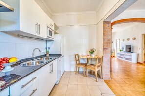 Une cuisine compacte avec un coin repas, des meubles blancs, un four à micro-ondes et un téléviseur en arrière-plan.