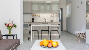 A modern kitchen with white cabinets, a dining table with chairs, and a fruit bowl on the table. - Glaros Homes (Chania)