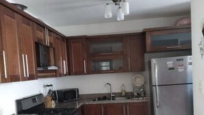 A kitchen with wooden cabinets, a stainless steel refrigerator, a microwave, and a gas stove. - GET AWAY Condo (Santiago De Los Caballeros)
