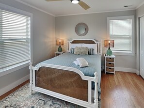 Een slaapkamer met een bed, twee nachtkastjes, een plafondventilator en een raam met zonwering.