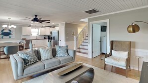 Un salon moderne avec un canapé, une table basse et un fauteuil. Un escalier mène à un autre niveau.