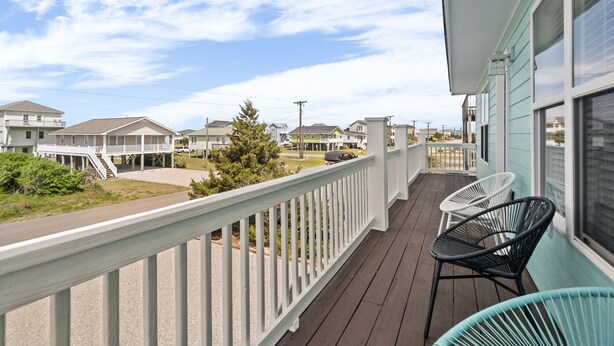 Un balcon avec des balustrades blanches, un immeuble turquoise et une vue sur d’autres maisons.