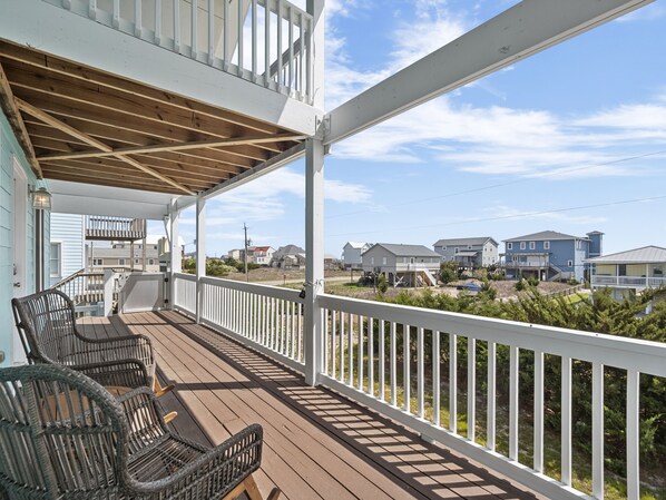 A wooden deck with white railings, wicker chairs, and a view of neighboring houses. - Pickens Paradise | Pet Friendly + Ocean View Deck! (Topsail Beach)