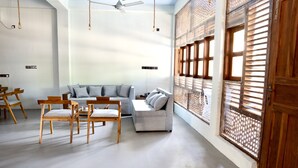 Un salon moderne avec un canapé gris, des chaises en bois, un ventilateur de plafond et une grande fenêtre dotée de stores en bois.