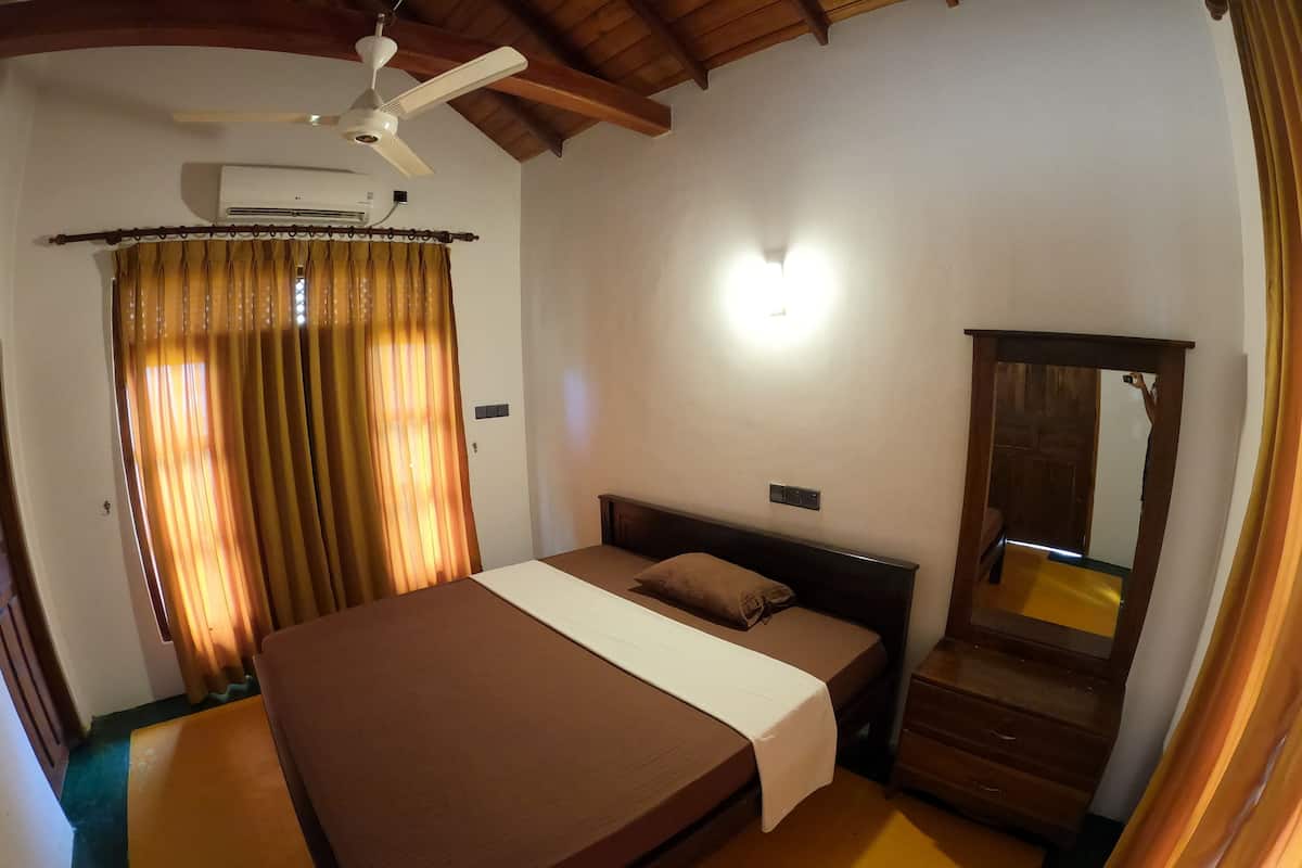 Un dormitorio con una cama grande, ventilador de techo, aire acondicionado, espejo y cortinas.