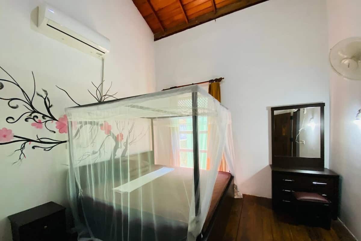 Un dormitorio con cama con dosel, cómoda, espejo y aire acondicionado.
