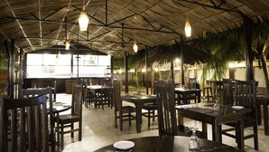 Un espace de restauration intérieur doté de nombreuses tables et chaises, d’un plafond haut avec des poutres apparentes et de luminaires suspendus.