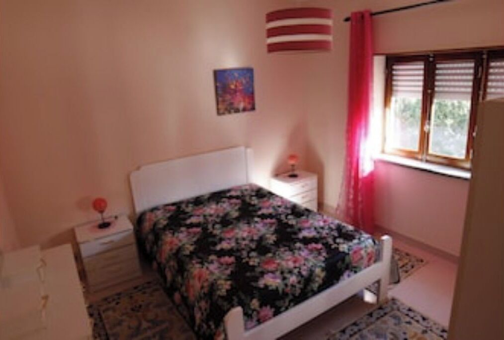 A bedroom with a bed, a nightstand, a window with blinds, and a wall-mounted flag.