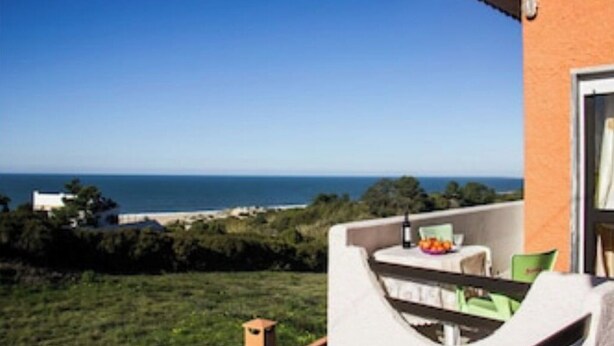 A balcony with a table and chairs, overlooking a coastal view. - Casa Milu - (Nazaré)