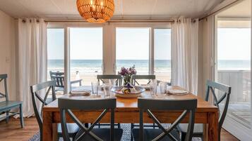 A dining area with a view of the beach, a hanging light fixture, and a table set for two.