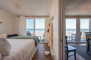 Habitación de hotel con cama, vista a la playa, zona de estar con mesa y sillas, y perchero.
