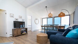 Una sala de estar con televisor, sofá y comedor con vista al océano.