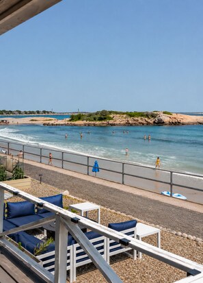 A beach with a wooden deck, seating, and a view of the ocean.