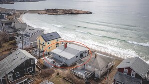 Una zona residencial costera con casas cerca de la playa, un promontorio rocoso y un faro a lo lejos.