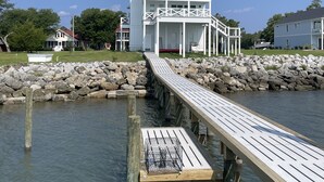 Une propriété située au bord de l’eau, avec une jetée en bois menant à une maison blanche dotée d’un balcon.