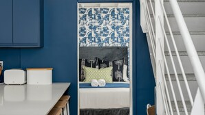 Een compact appartement in moderne stijl, met een keuken, een eettafel met barstoelen, een stapelbed met behang met een patroon, en een trap.