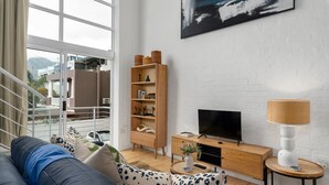 Een moderne woonkamer met een bank, een houten boekenkast, een televisie en een lamp.