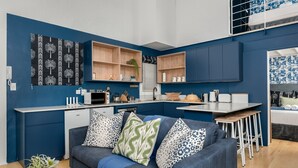 Een moderne keuken met inbouwplanken, een eethoek met een barkruk, en een woonkamer met een bank en decoratieve kussens.
