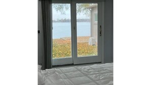 A bedroom with a large window and sliding glass door, offering a view of a lake and autumn foliage.