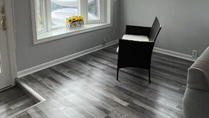 A room with grey walls, two windows with white frames, a black chair, and a grey couch.