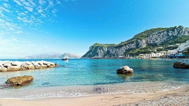 A coastal beach with clear blue water, rocky formations, and a mountainous backdrop. - Capri Charming mediterranean apartment (Marina Grande)