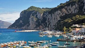 A coastal marina with boats docked, a rocky cliff in the background, and buildings along the shore. - Capri Charming mediterranean apartment (Marina Grande)