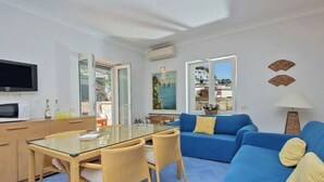 A modern living room with a glass dining table, blue sofa, and wicker chairs. - Capri Charming mediterranean apartment (Marina Grande)