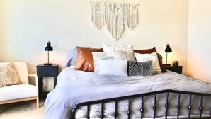 A bedroom with a bed, two nightstands, a wall hanging, and a sofa.