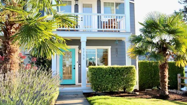 A two-story building with a balcony, a door with a number, and a well-maintained garden with palm trees and shrubs.