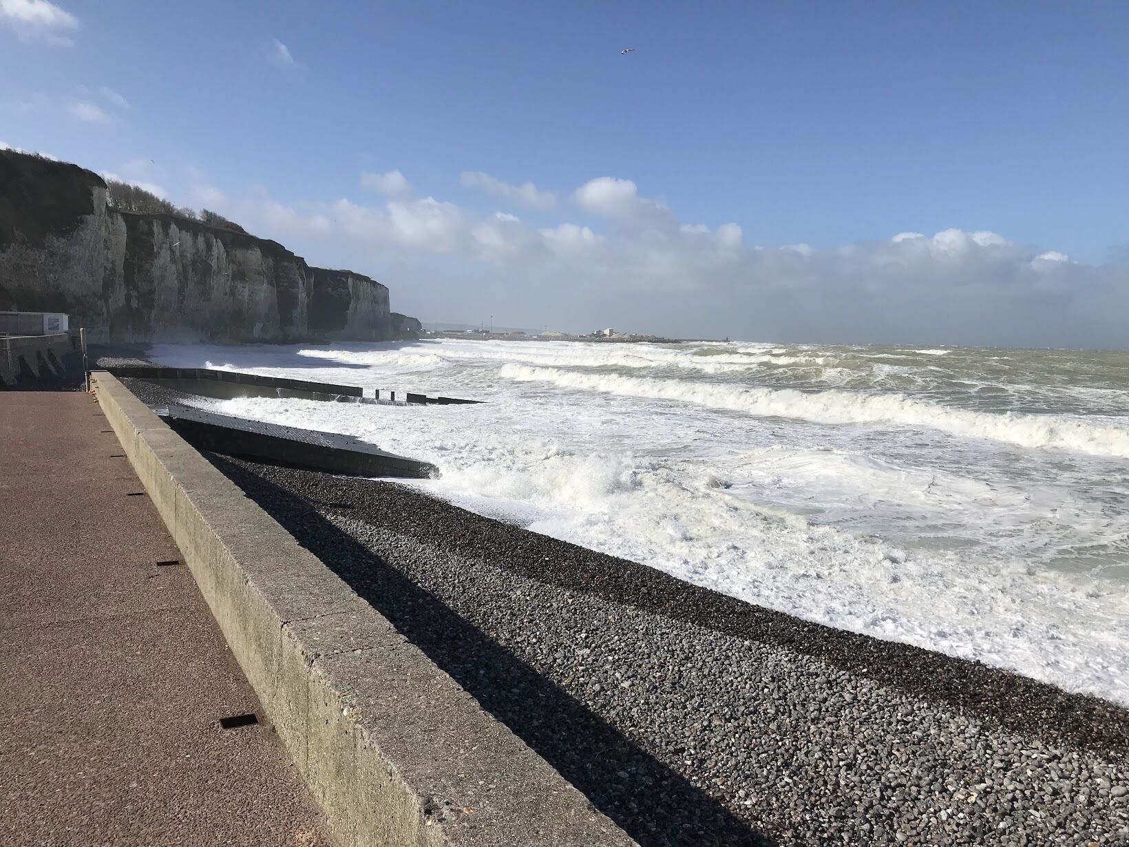 A rocky coastal walkway with a concrete barrier and waves crashing against it.