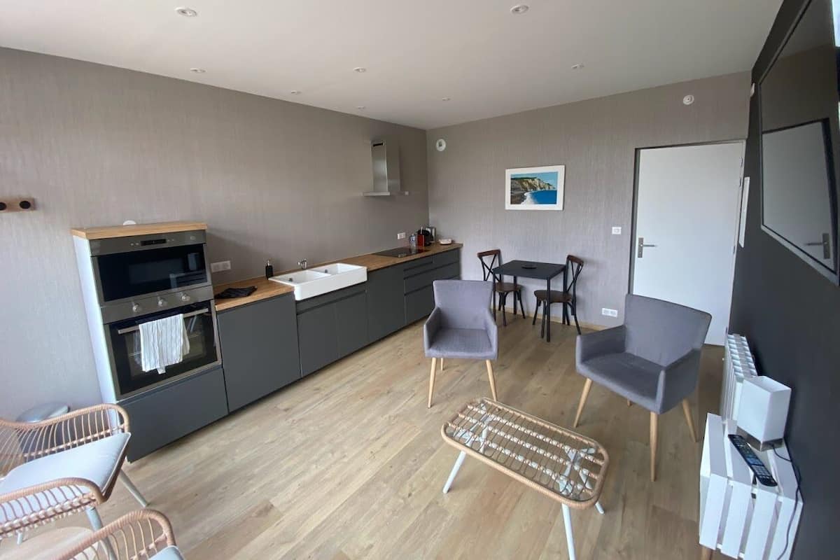 A modern kitchen with a built-in oven and sink, a dining area with two chairs, and a small table.