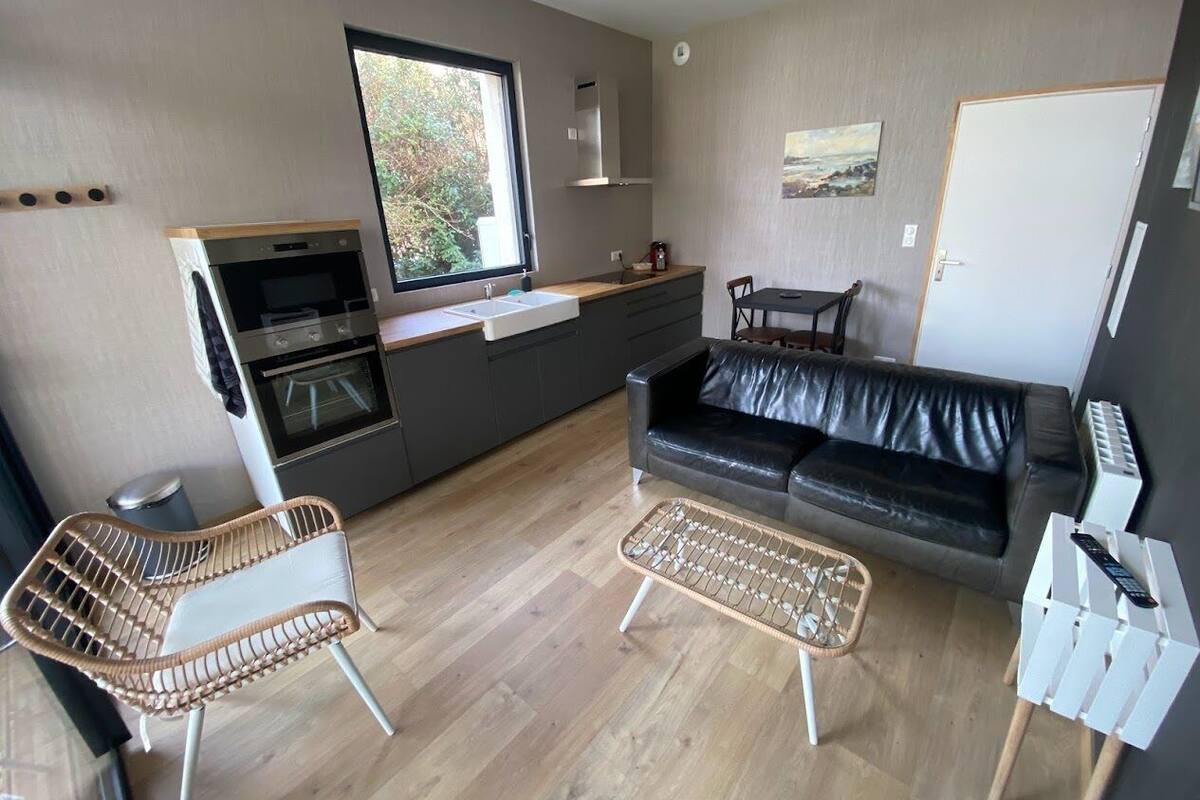 A modern kitchen with a built-in oven and microwave, a dining area with a black leather sofa, and a large window providing natural light.