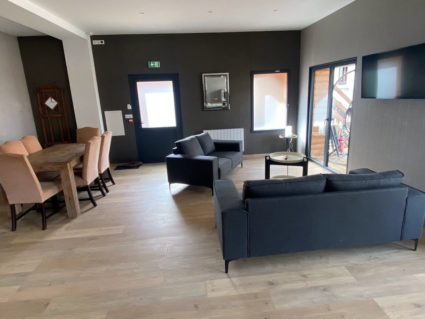 A modern living room with a wooden dining table, two sofas, and a TV mounted on the wall.
