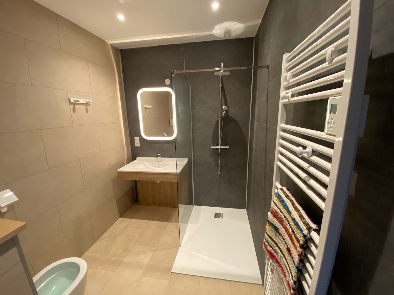 A modern bathroom with a glass-enclosed shower, a vanity with a mirror, and a towel rack with a folded towel.