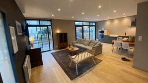 Una sala de estar moderna con sofá, mesa de centro y comedor con sillas. Se observa un área de cocina con mostrador y armarios.