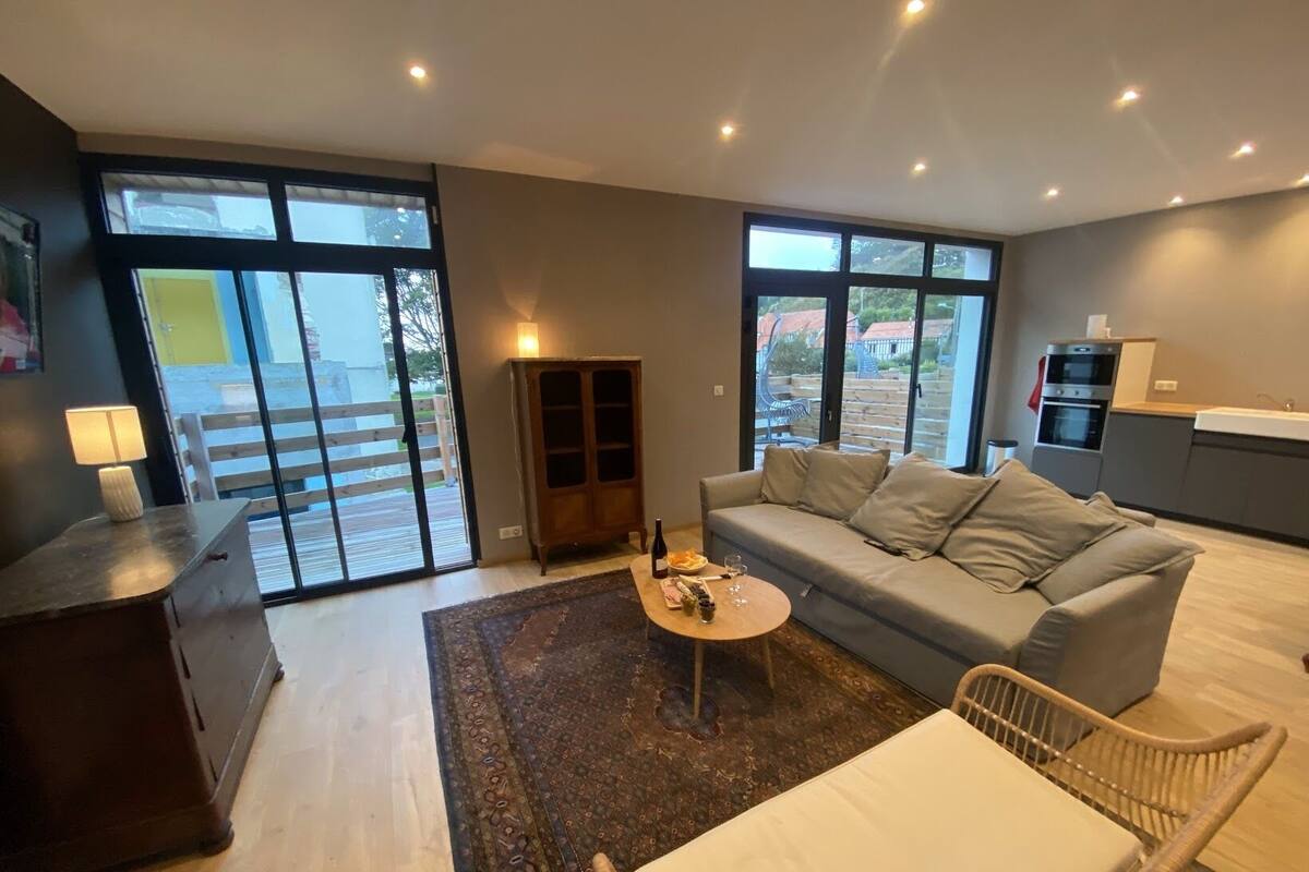 A modern living room with a sofa, coffee table, and a dining area with a kitchen in the background.