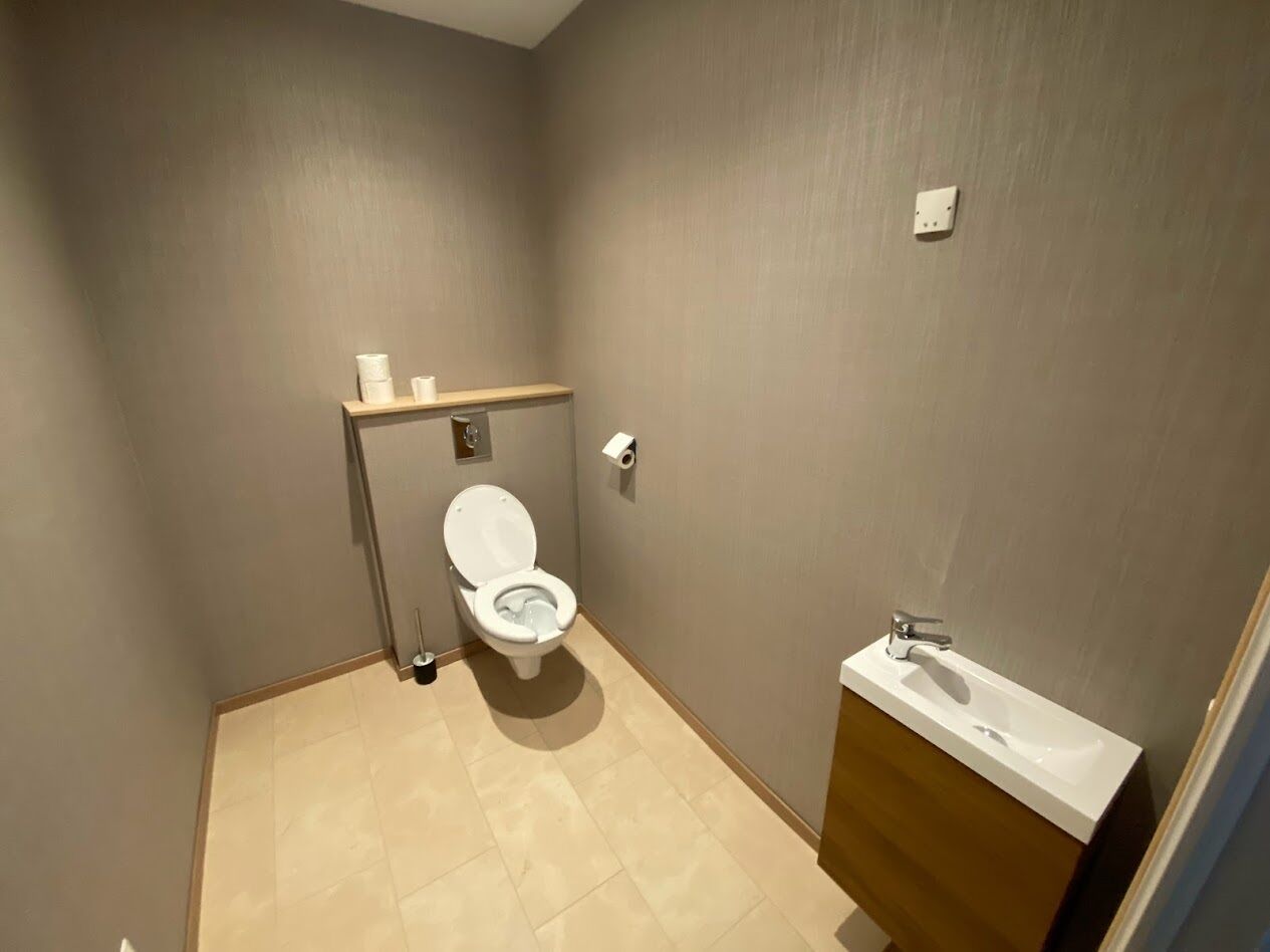 Une petite salle de bain compacte, équipée de toilettes, d’un lavabo et d’une étagère de rangement.