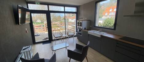 Eine moderne Küche mit großem Fenster, einem Essbereich mit Stühlen und Blick ins Freie.