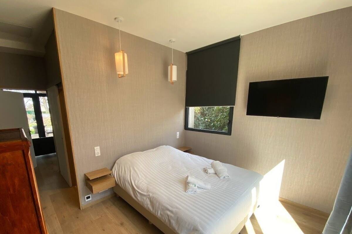 A modern bedroom with a large bed, bedside tables, a window, and a TV mounted on the wall.