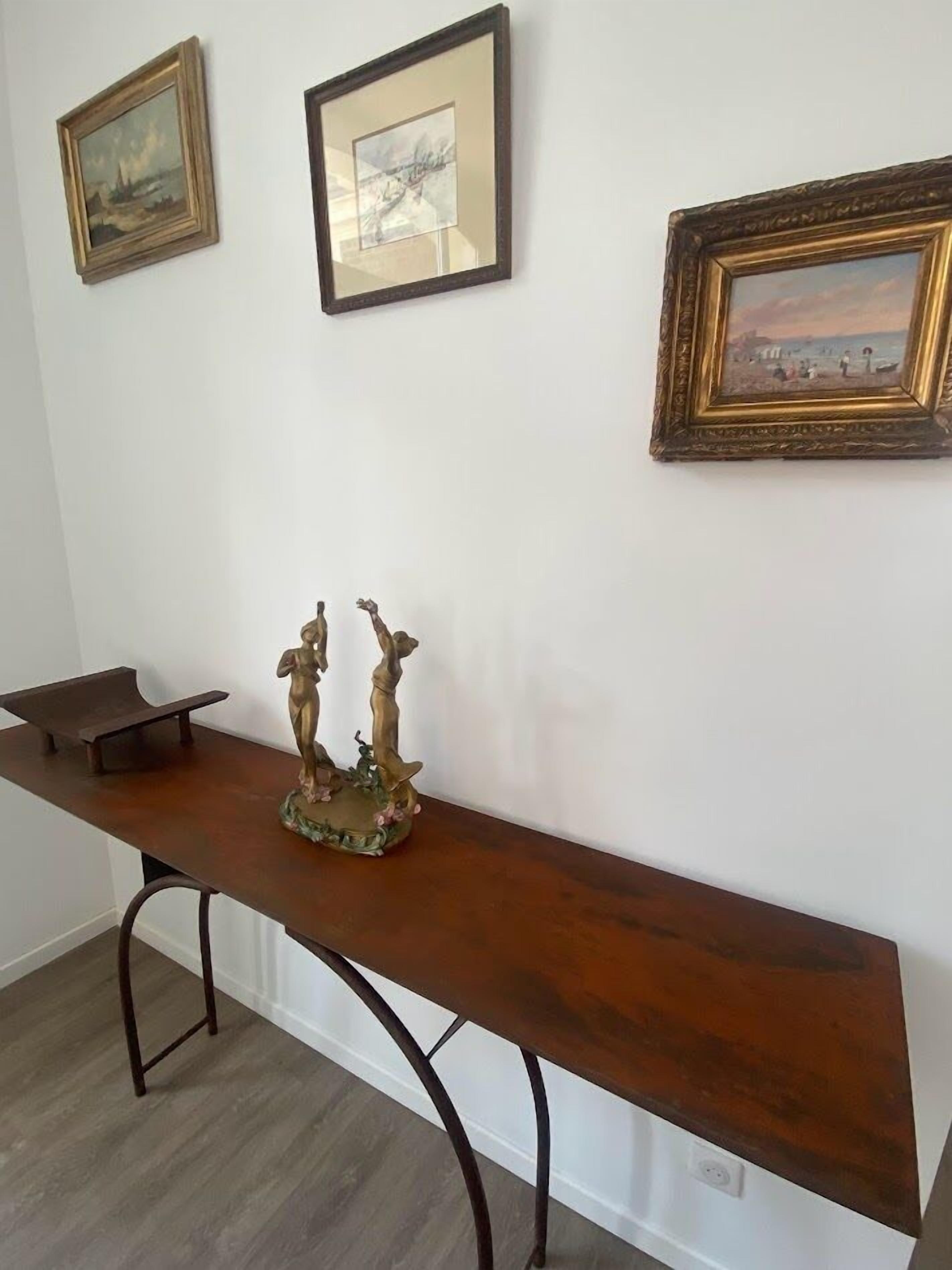 A room with a wooden bench, two framed artworks on the wall, and a small sculpture on the bench.